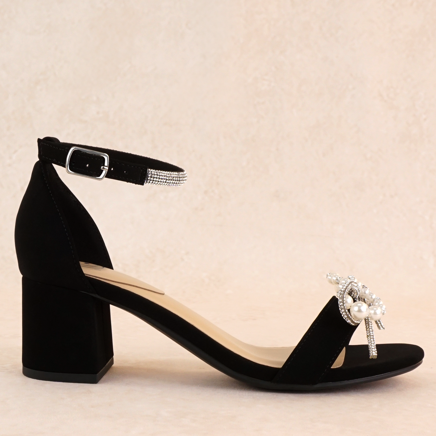 A black nubuck block heel with a pearl and rhinestone bow on a single strap across the toes and a rhinestone adjustable ankle strap