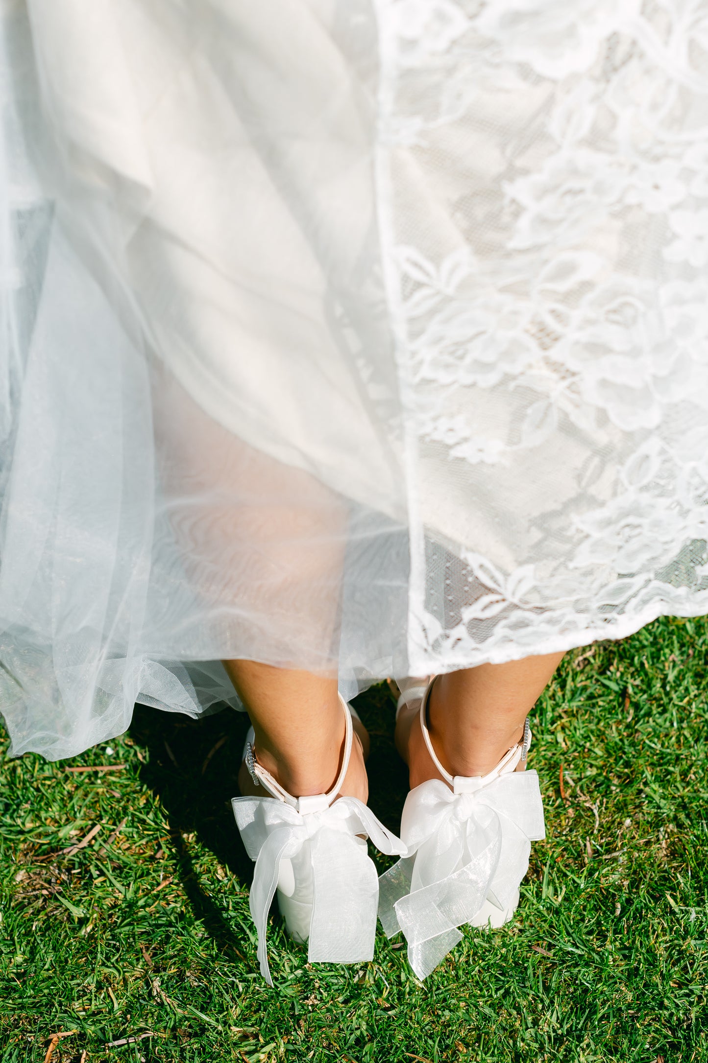 Wide fit simple low 2.5" block heel in white with a bow at the back worn by a woman in a white dress