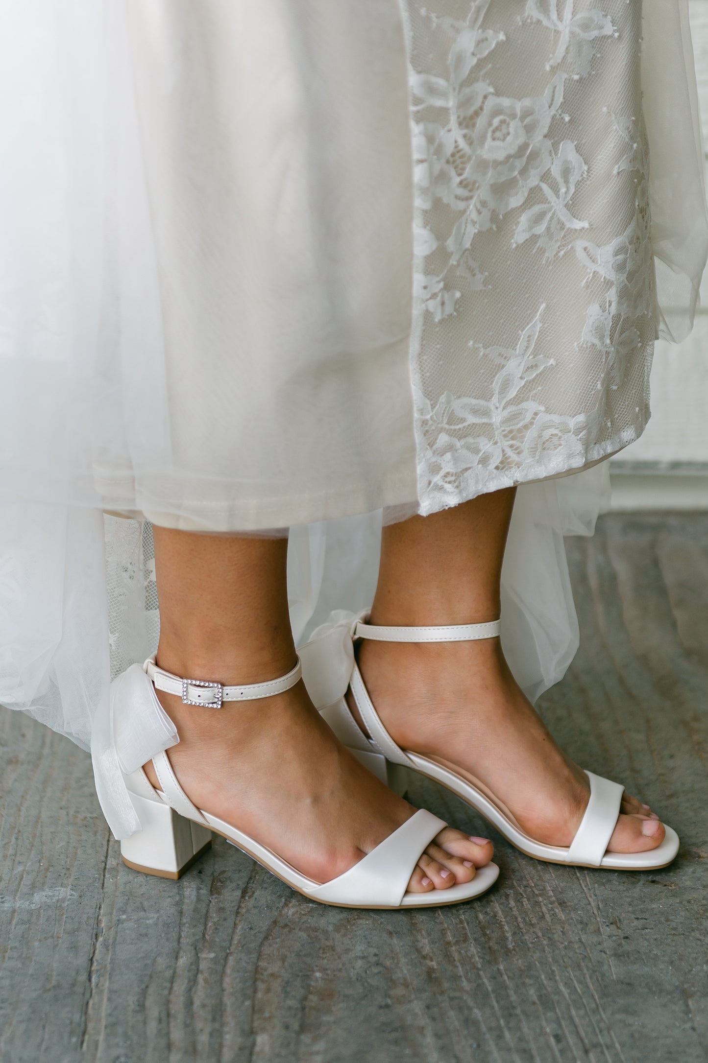 Wide fit simple low 2.5" block heel in white with a bow at the back worn by a woman in a white dress