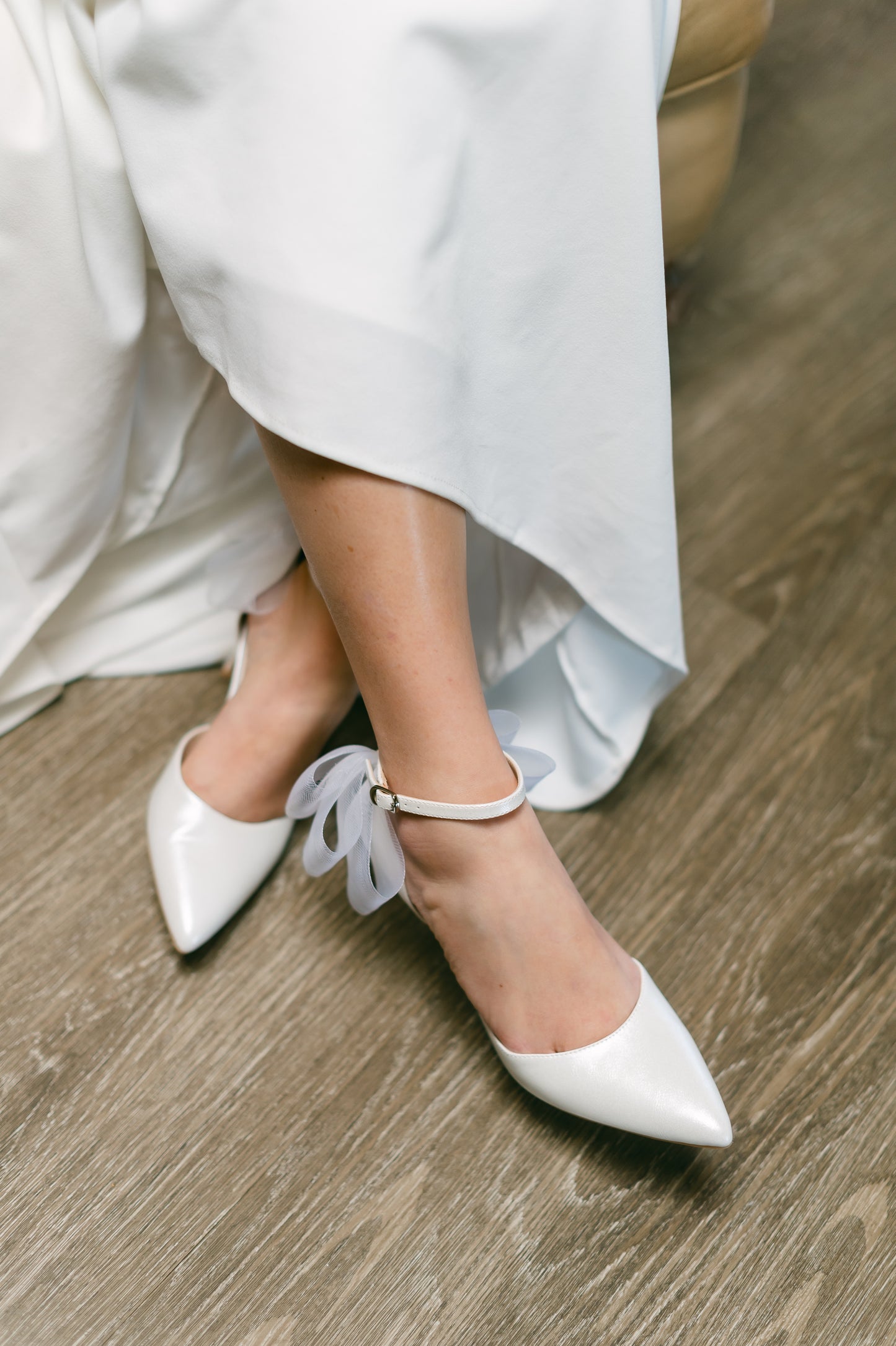 White d’orsay pump with ankle strap bow detail and a 3.25" stiletto heel worn by a woman in a white dress
