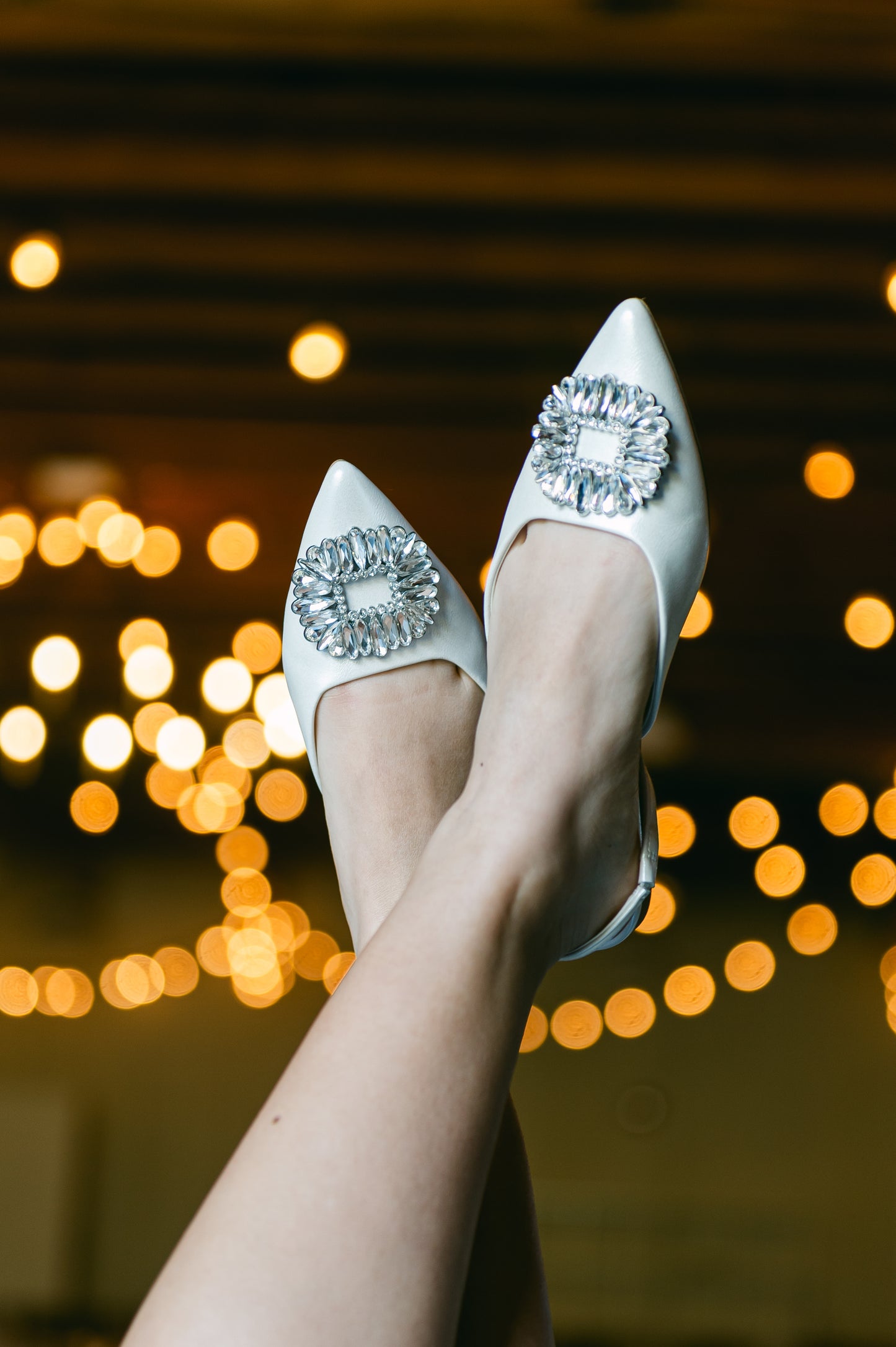 White pointed-toe slingback flat shoe with rhinestone accent being worn