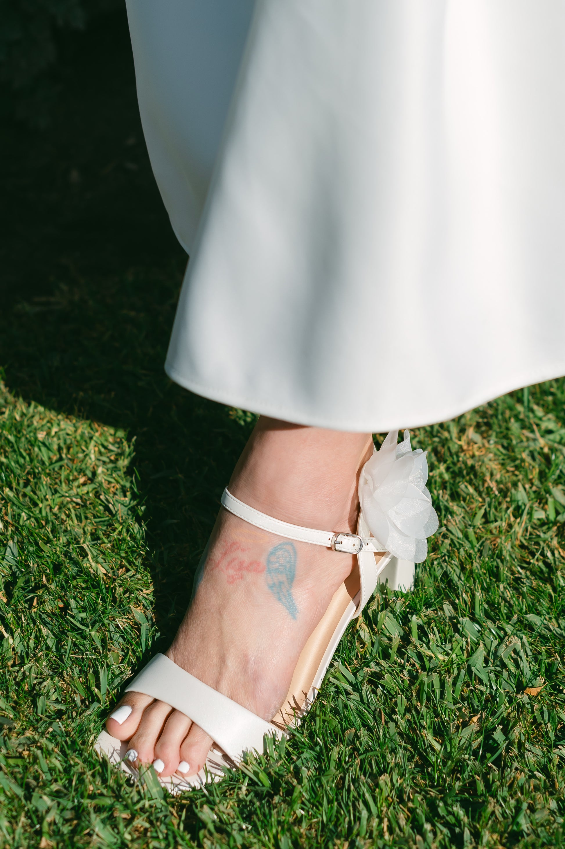 Flared 3" block heel in white with slim ankle strap and flower detail worn by a woman in a white dress