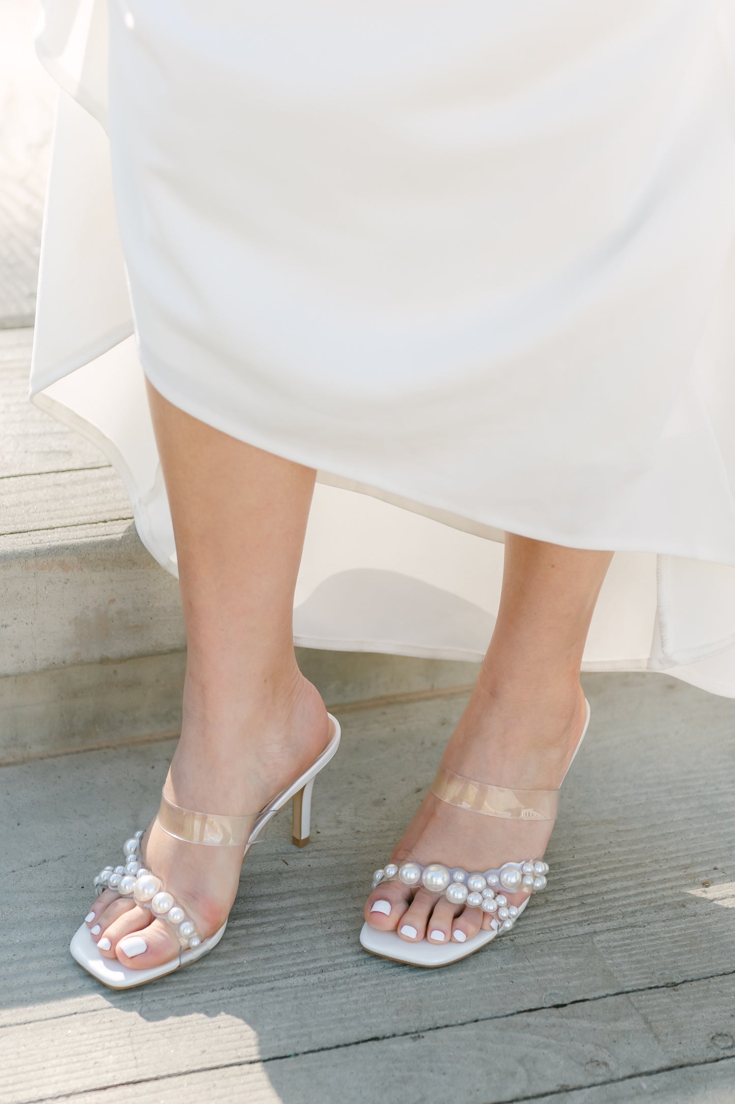 Stiletto slide with pearls on a lucite cross-strap with a 3.5" stiletto heel worn by a woman in a white dress