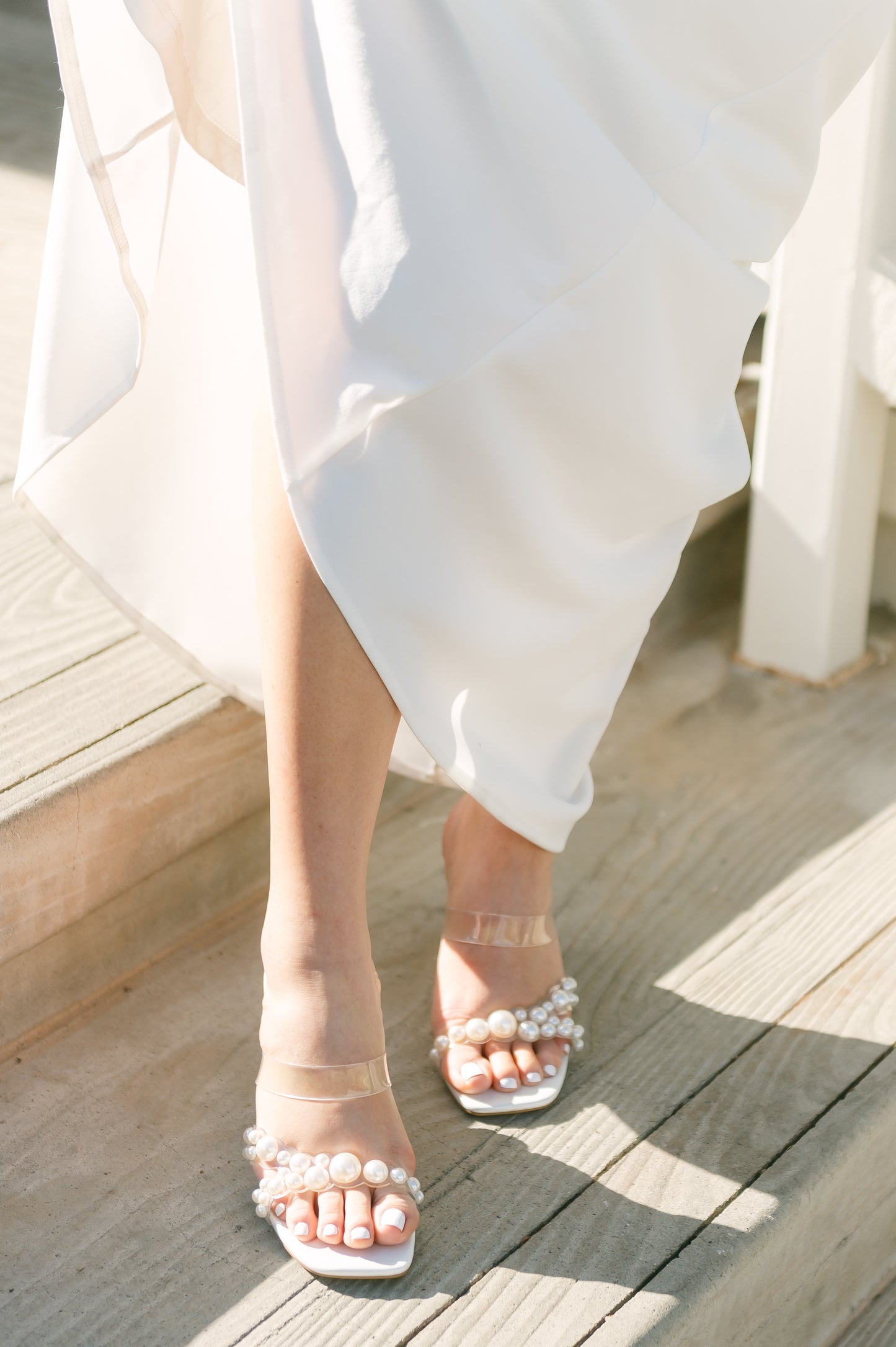 Stiletto slide with pearls on a lucite cross-strap with a 3.5" stiletto heel worn by a woman in a white dress