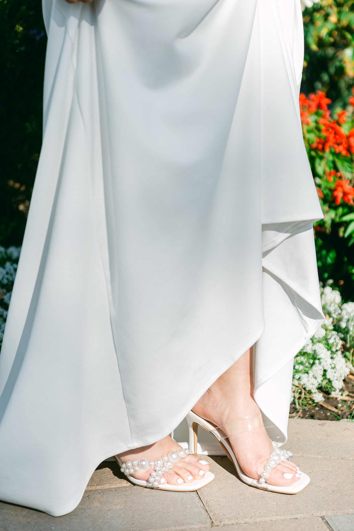 Stiletto slide with pearls on a lucite cross-strap with a 3.5" stiletto heel worn by a woman in a white dress