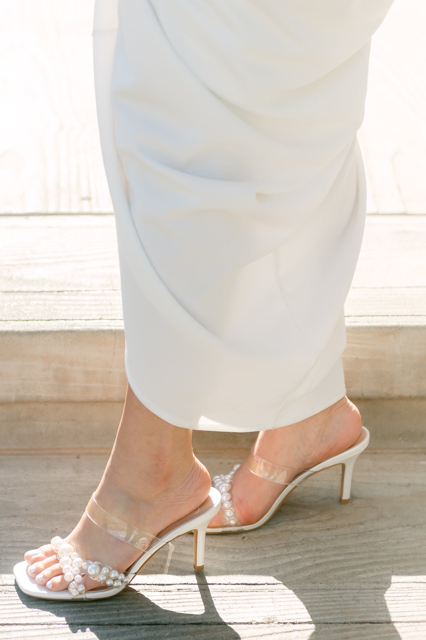 Stiletto slide with pearls on a lucite cross-strap with a 3.5" stiletto heel worn by a woman in a white dress