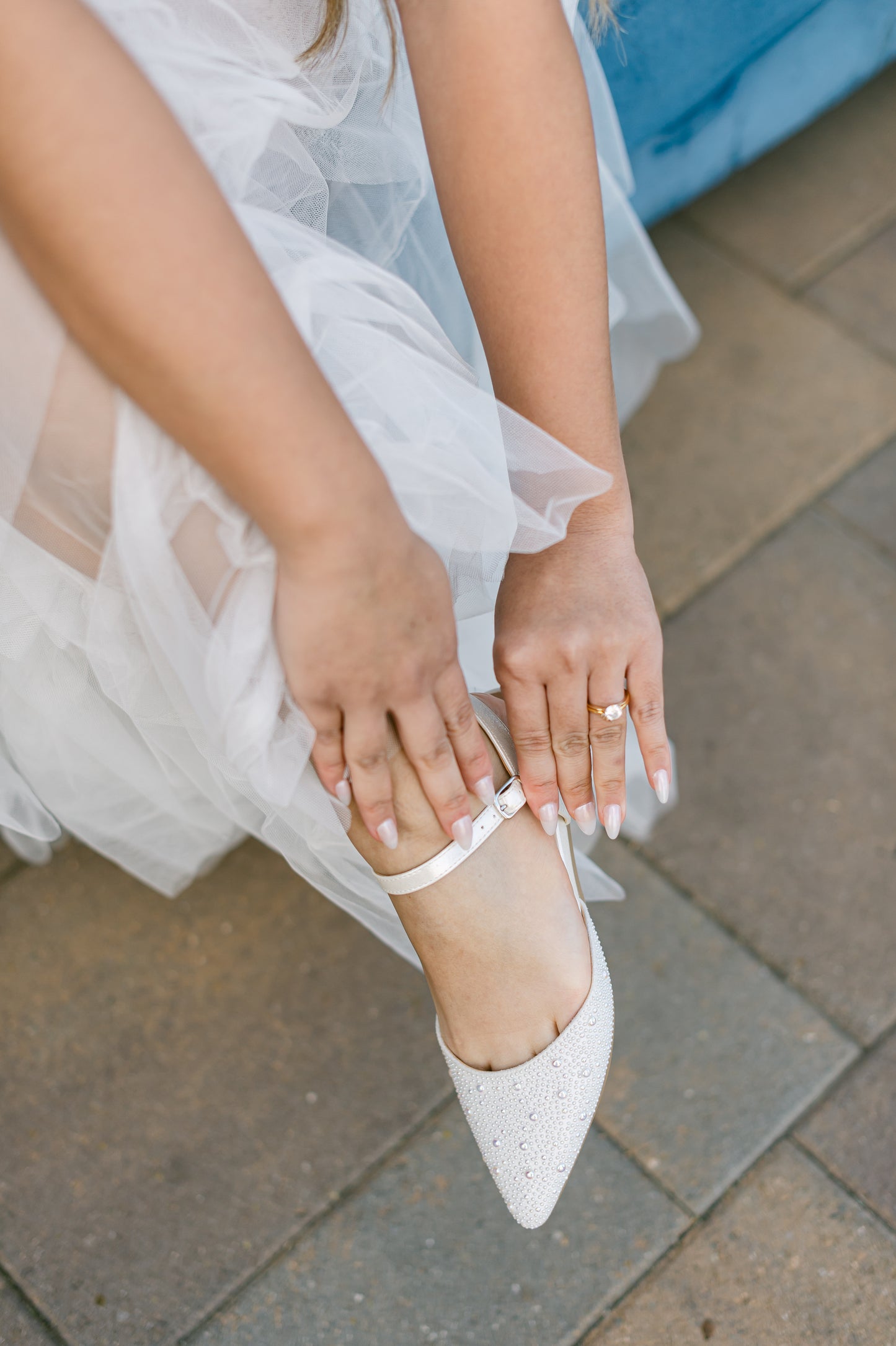 Ankle strap open-heeled white flat with allover pearls worn by a woman in a white dress