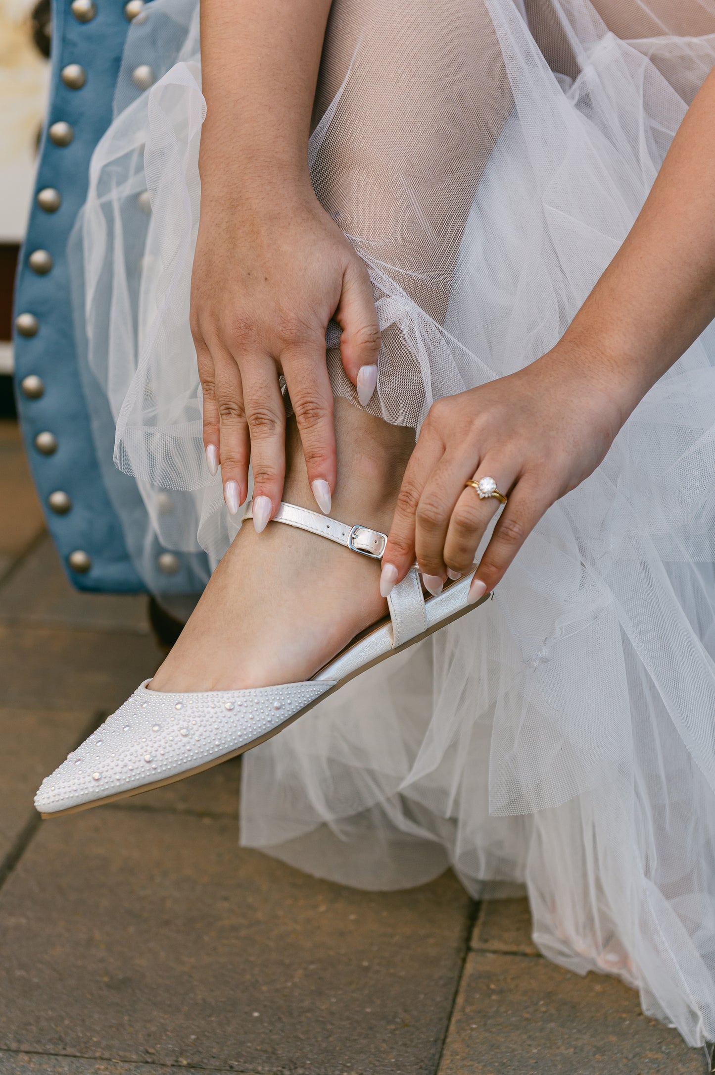 Ankle strap open-heeled white flat with allover pearls worn by a woman in a white dress