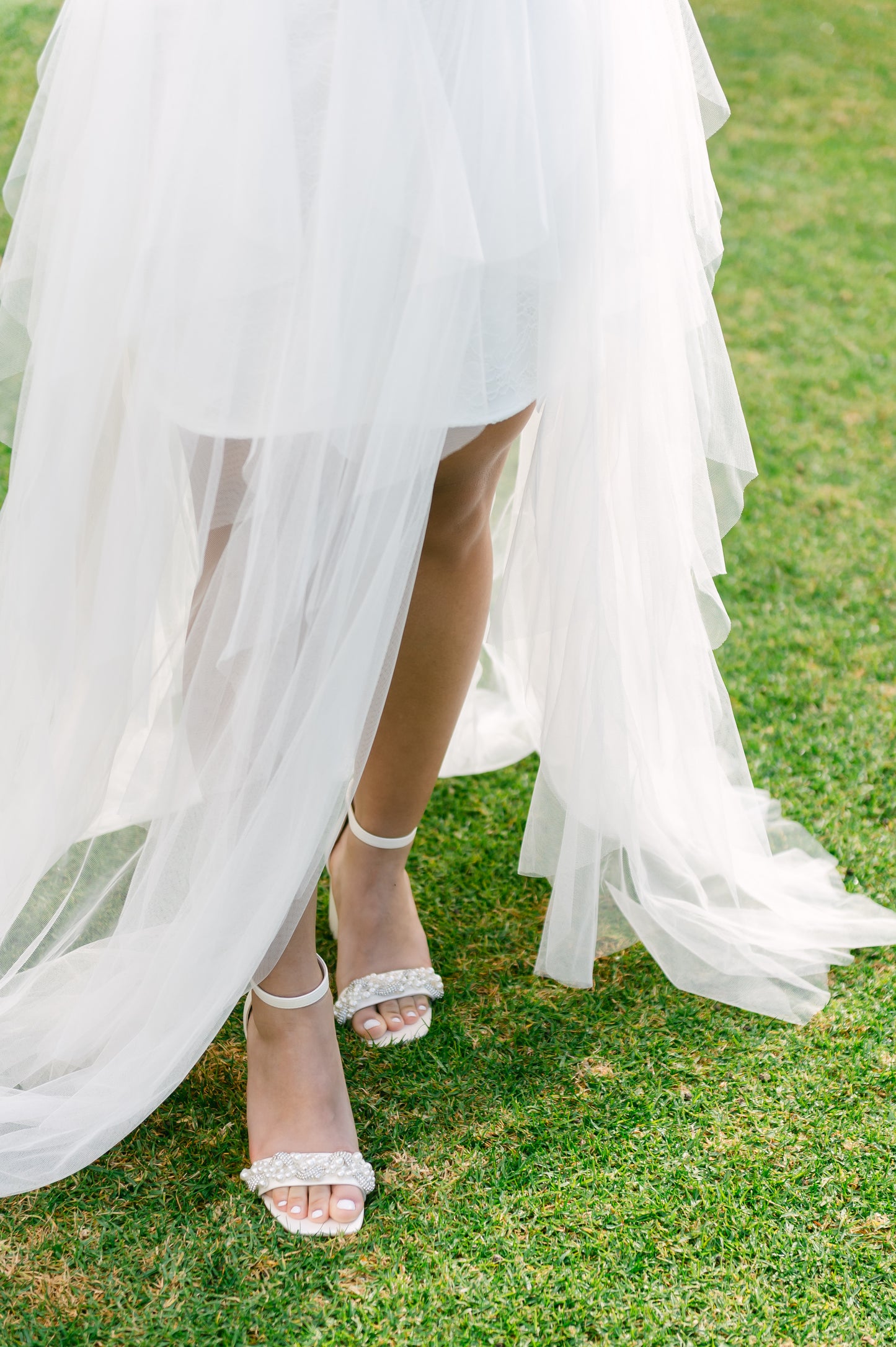 Pearls and rhinestones intertwined on a wide fit single-band 3.25" ankle strap block heel worn by a woman in a white dress