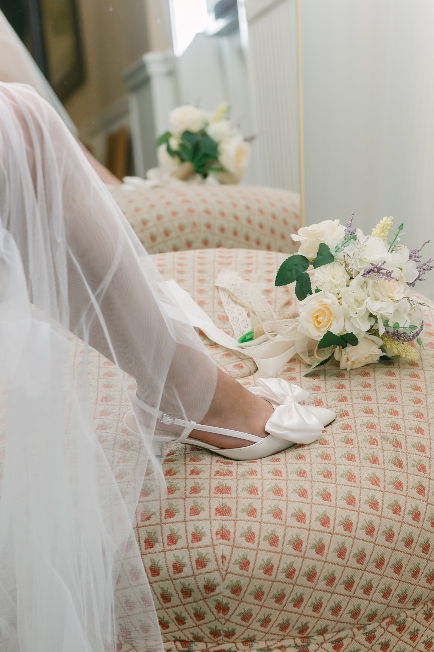Classic white 2.25" kitten heel adjustable slingback with a satin bow worn by a woman in a white dress