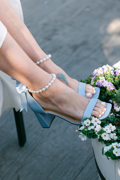 3" flared block heel in blue with adjustable pearl ankle strap and satin ribbon tie worn by a woman in a white dress