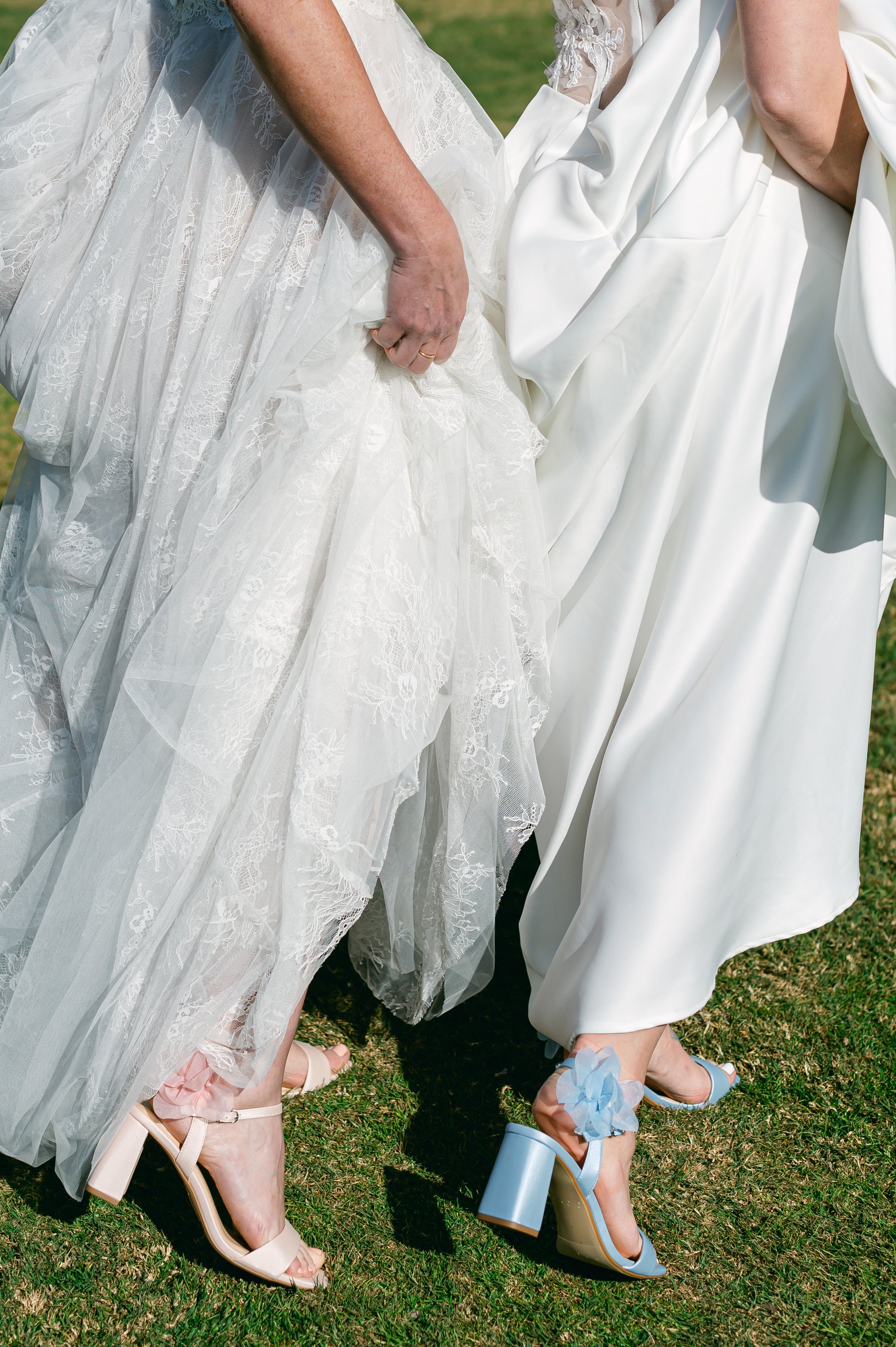 Flared 3" block heels in blue and pink with slim ankle strap and flower detail worn by two women in white dresses