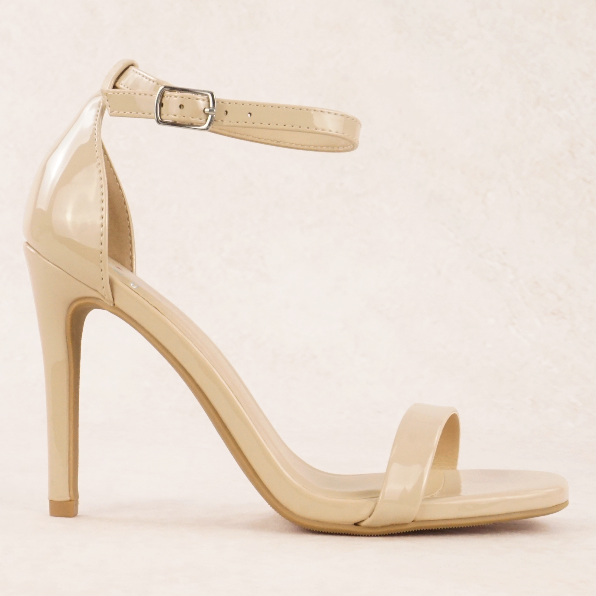A dark beige patent material stiletto heel with adjustable ankle strap