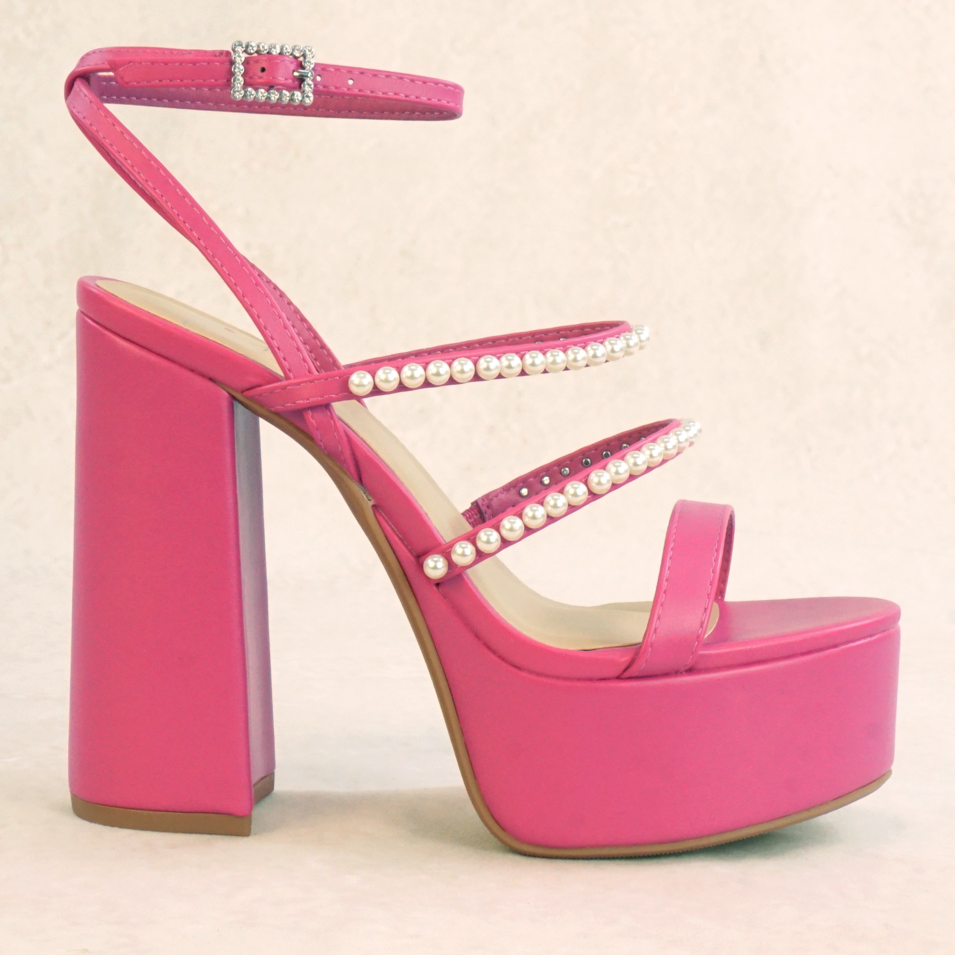 A fuchsia pink platform heel with adjustable ankle strap, rhinestone buckle and pearl straps