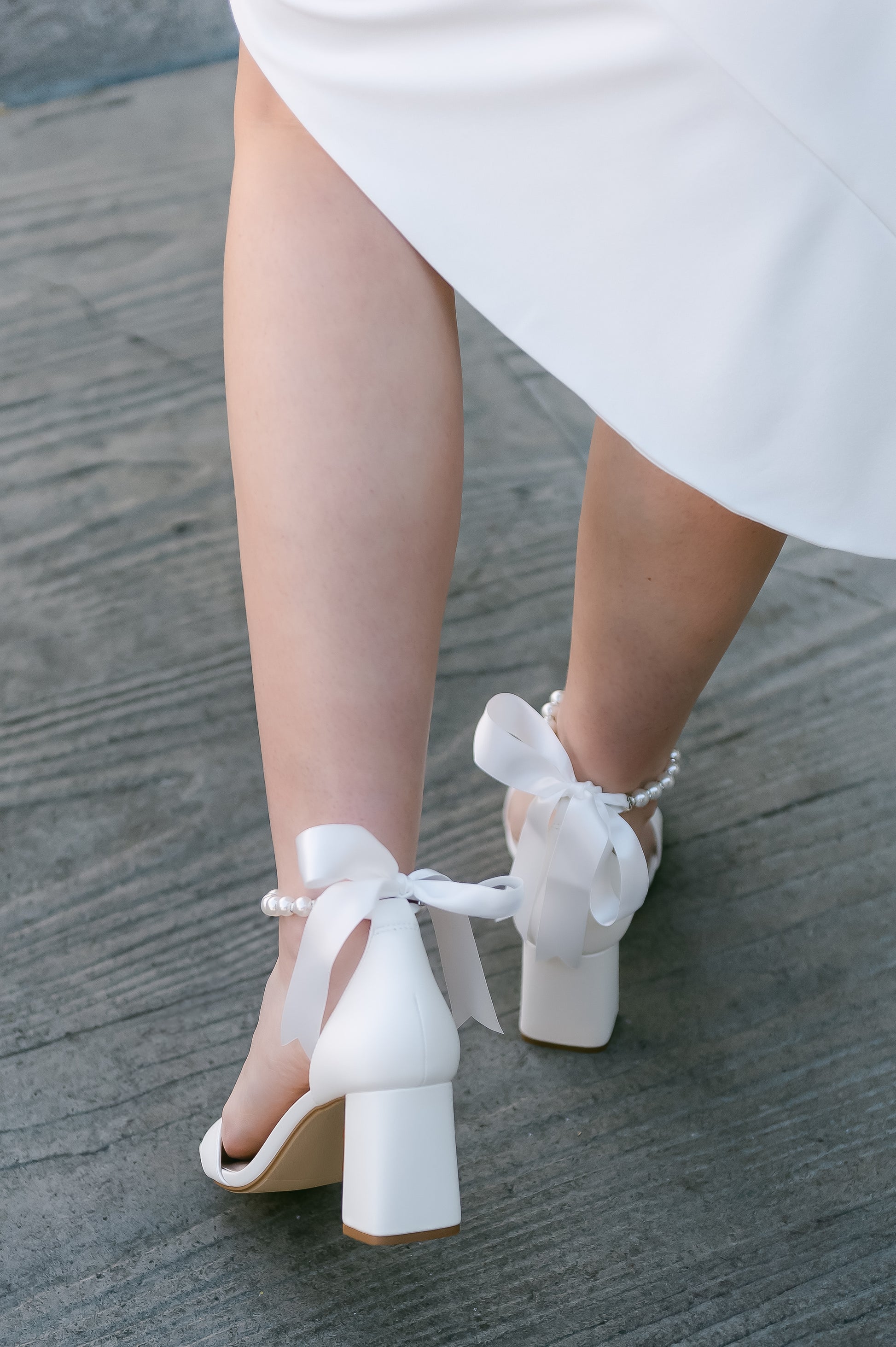 3" flared block heel in white with adjustable pearl ankle strap and satin ribbon tie worn by a woman in a white dress