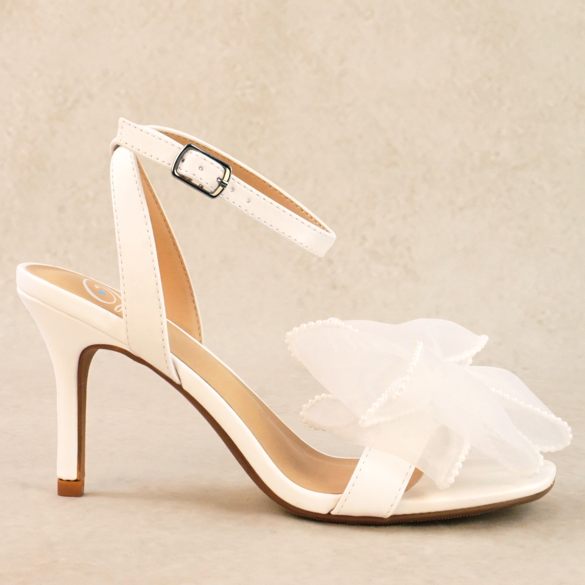 A white pearlescent stiletto heel with a pearl studded mesh bow and adjustable ankle strap
