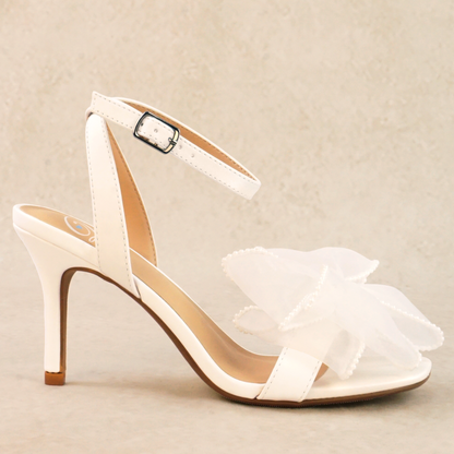 A white pearlescent stiletto heel with a pearl studded mesh bow and adjustable ankle strap