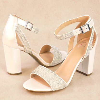 A pair of white pearlescent block heels with pearls and rhinestones and adjustable ankle strap
