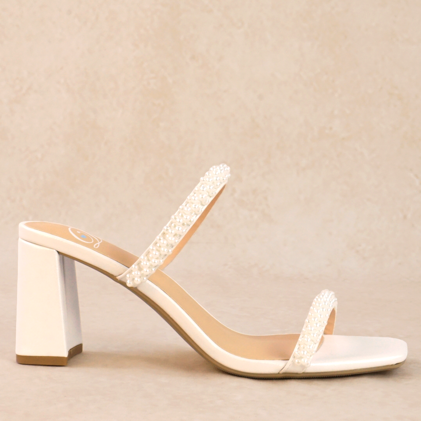 A white block heeled sandal with a pearlescent finish and pearl detailing on the straps