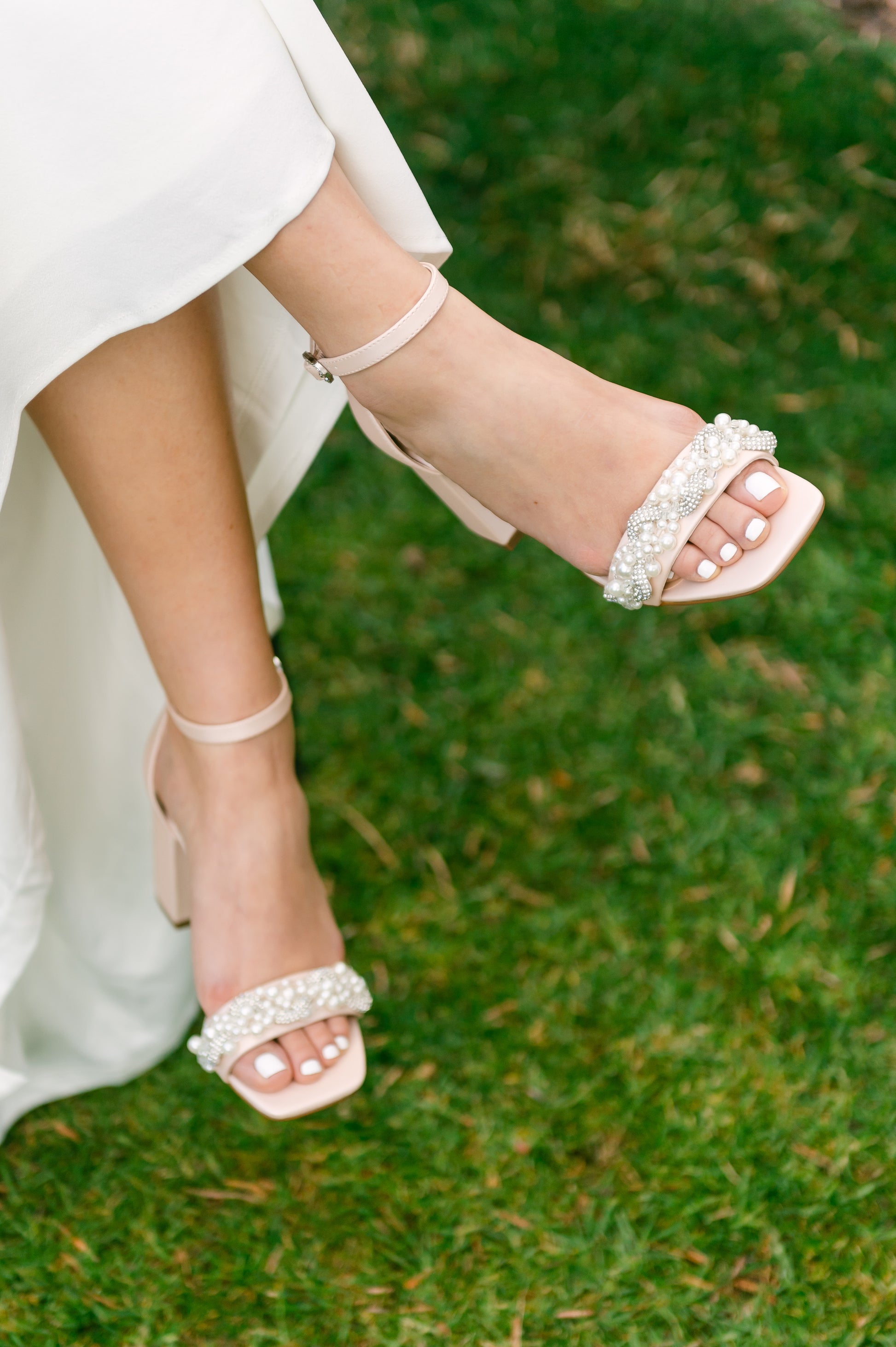 Pearls and rhinestones intertwined on a pink single-band 3.25" ankle strap block heel worn by a woman in a white dress