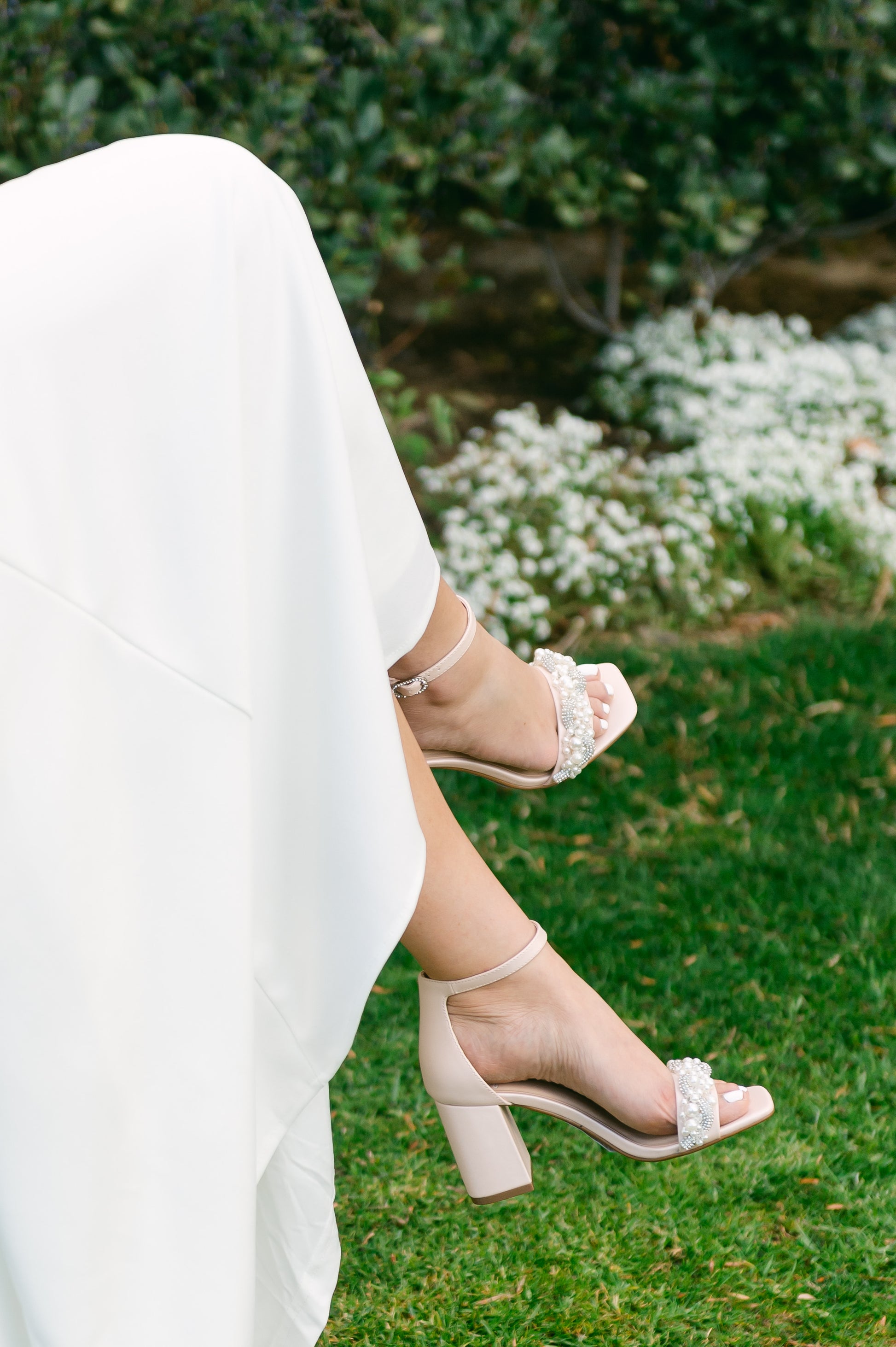Pearls and rhinestones intertwined on a pink single-band 3.25" ankle strap block heel worn by a woman in a white dress