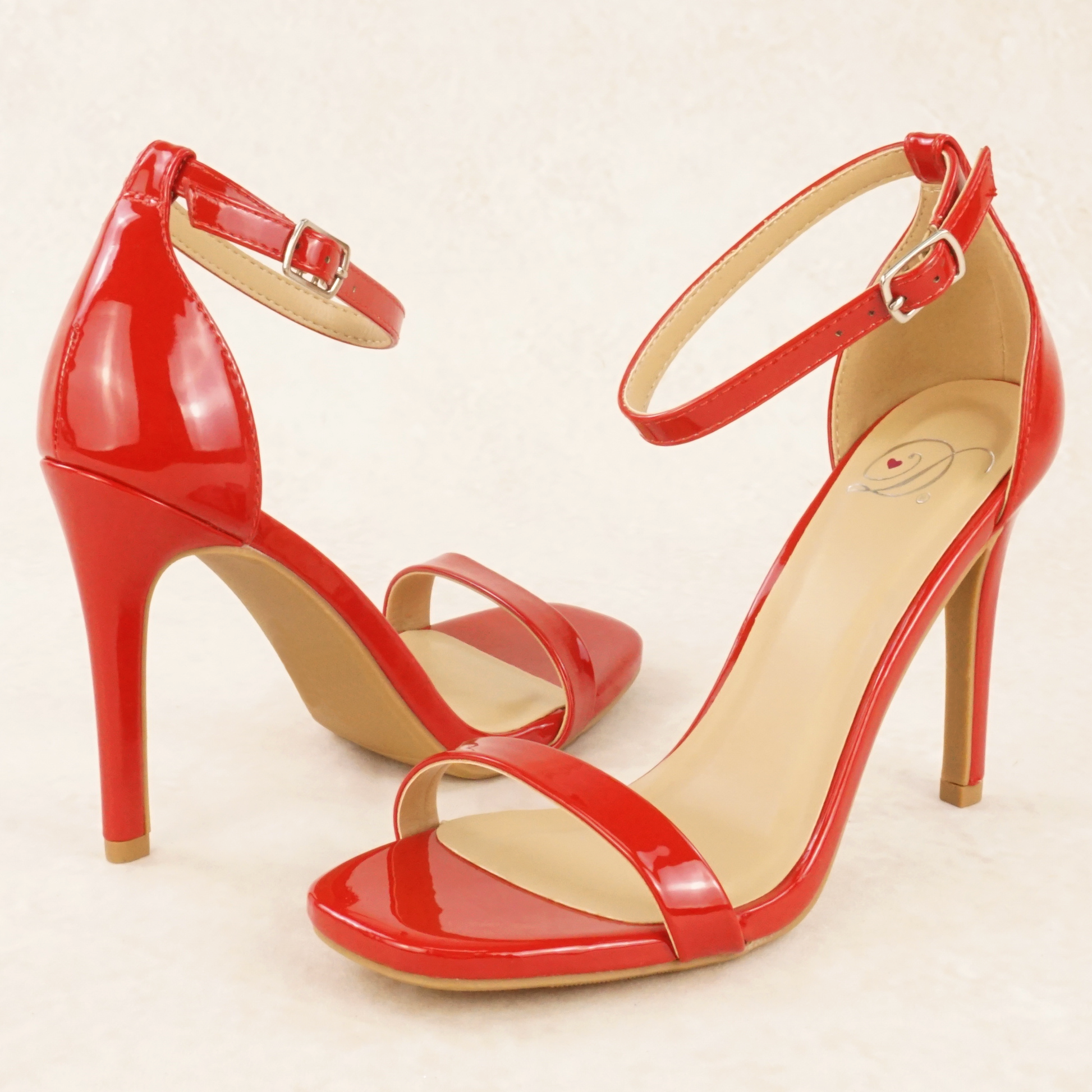 A pair of red patent material stiletto heels with adjustable ankle straps