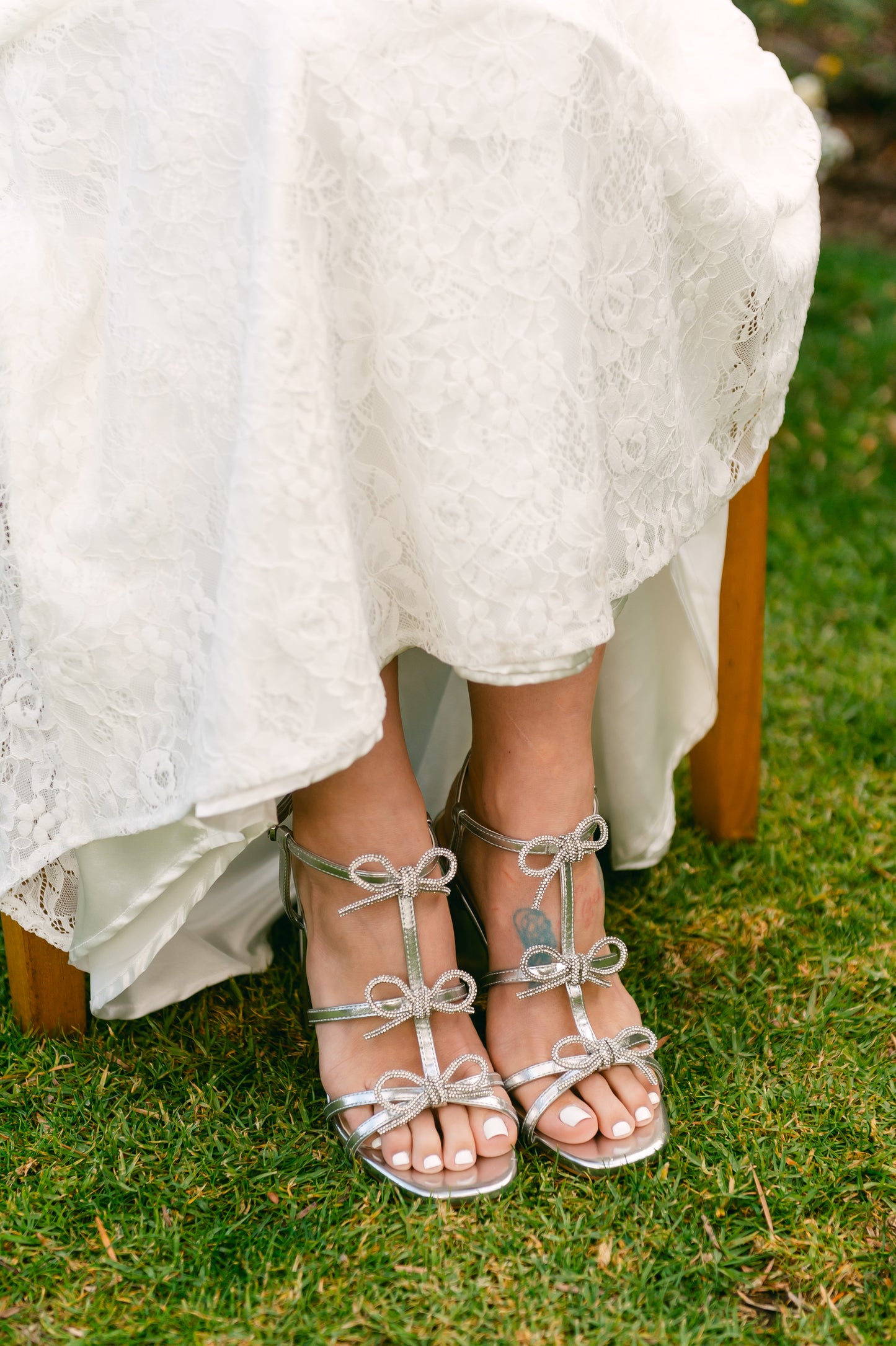 Rhinestone bows on a 4.25" block heel in metallic silver worn by a woman wearing a white dress
