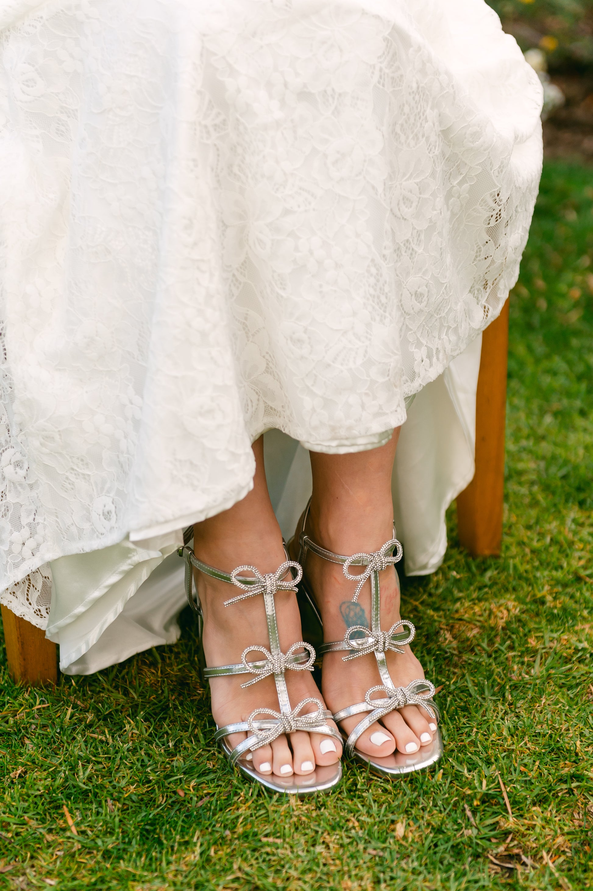 Rhinestone bows on a 4.25" block heel in metallic silver worn by a woman wearing a white dress