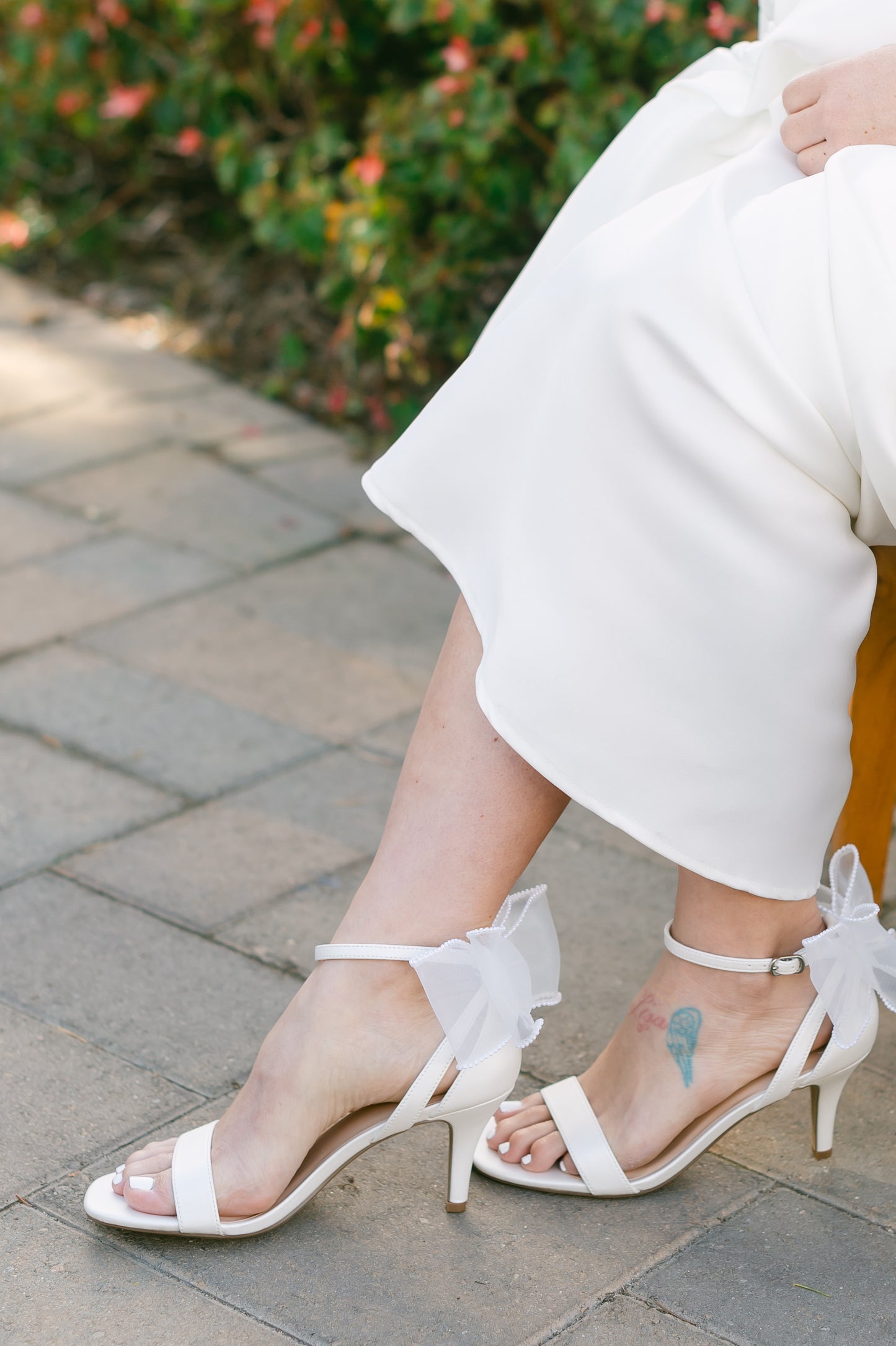 Wide fit simple single-band 3" stiletto heel in white with a beaded bow on the back worn by a woman in a white dress