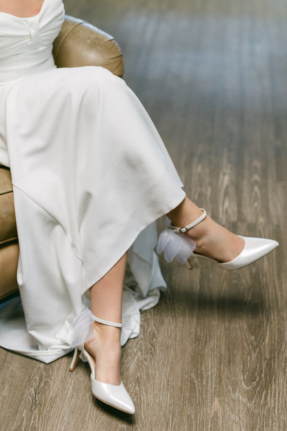 White d’orsay pump with ankle strap bow detail and a 3.25" stiletto heel worn by a woman in a white dress