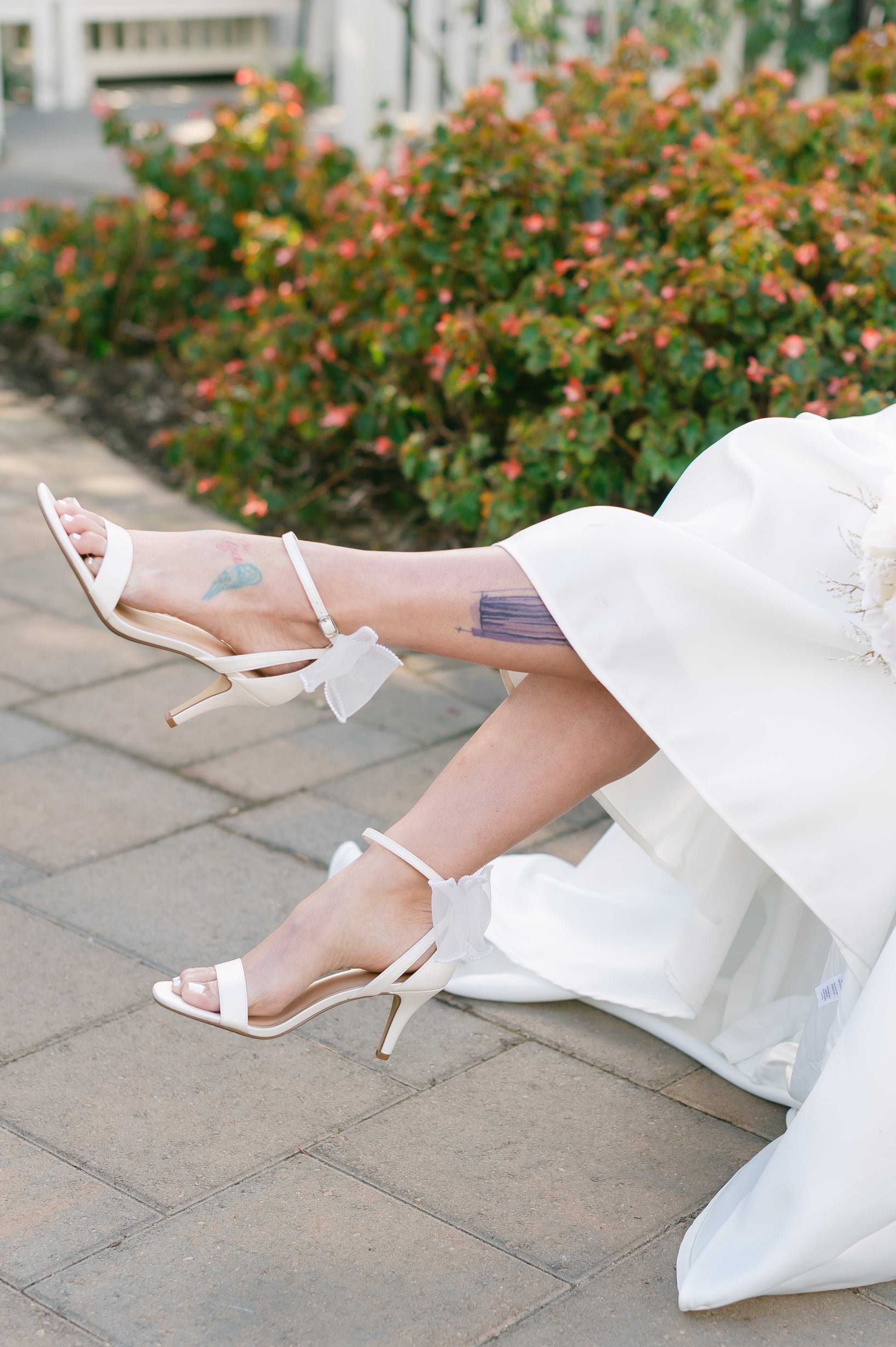 Wide fit simple single-band 3" stiletto heel in white with a beaded bow on the back worn by a woman in a white dress