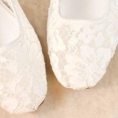 A pair of white flat shoes with floral lace pattern allover and Mary Jane style elastic strap