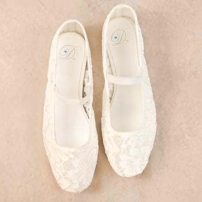 A pair of white flat shoes with floral lace pattern allover and Mary Jane style elastic strap