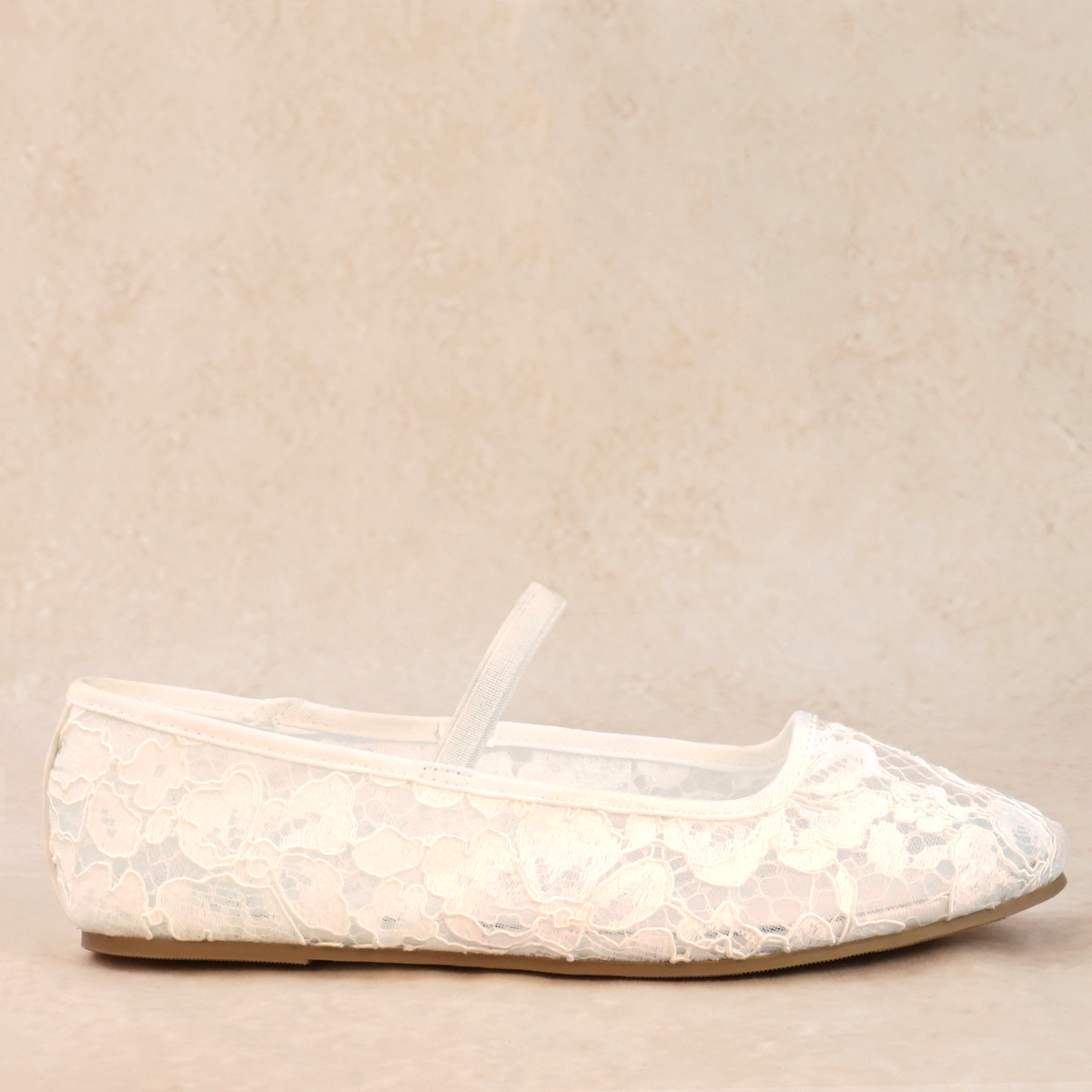 A white flat shoe with floral lace pattern allover and Mary Jane style elastic strap