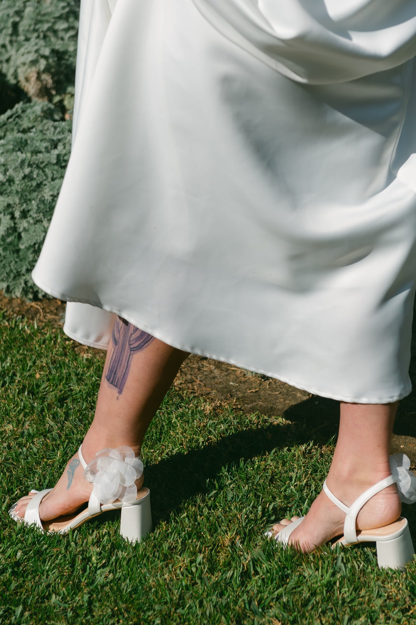 Flared 3" block heel in white with slim ankle strap and flower detail worn by a woman in a white dress