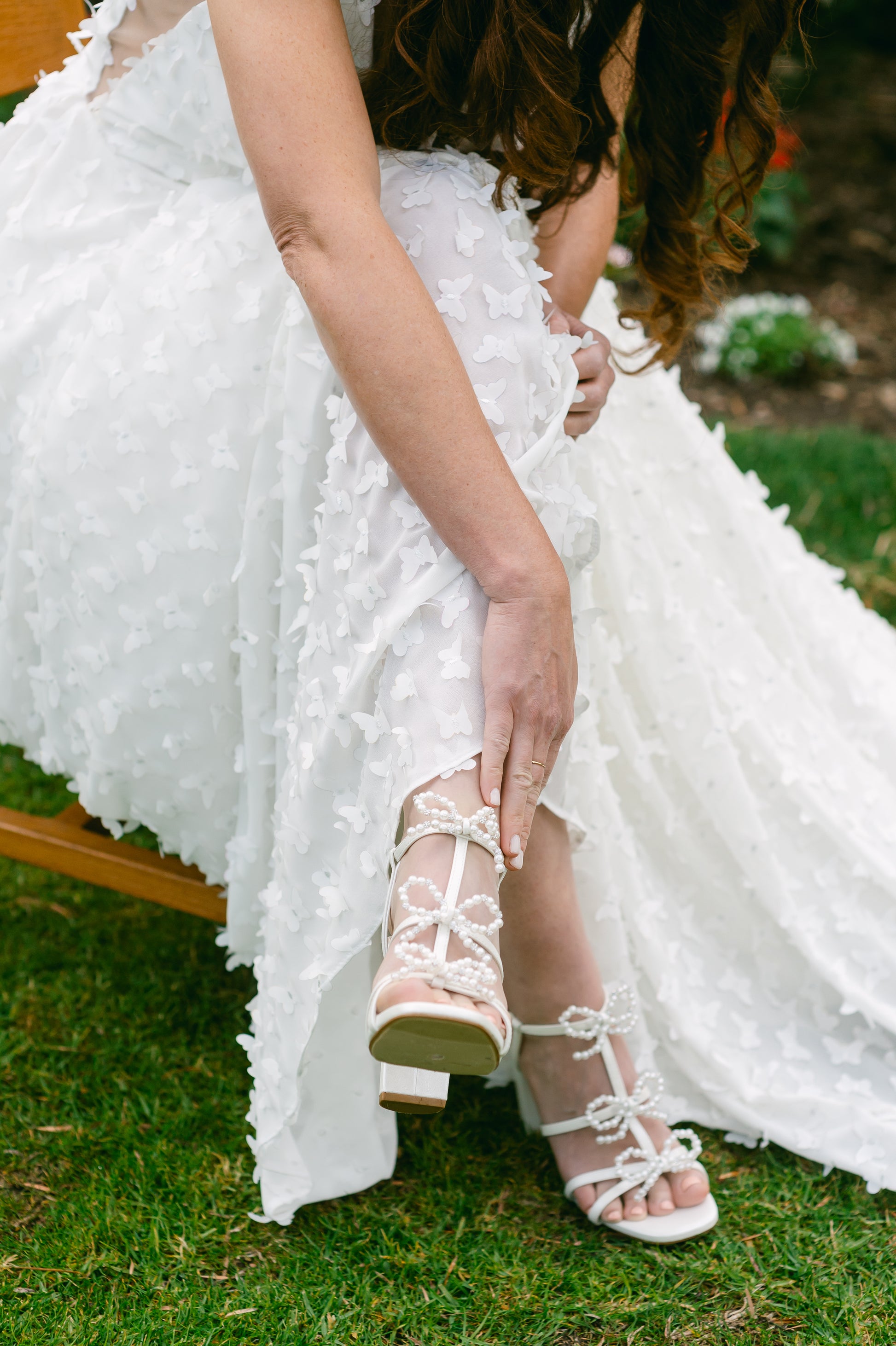 Pearl and rhinestone bows adorn a 4.25" block heel in pearlescent white worn by a woman in a white dress