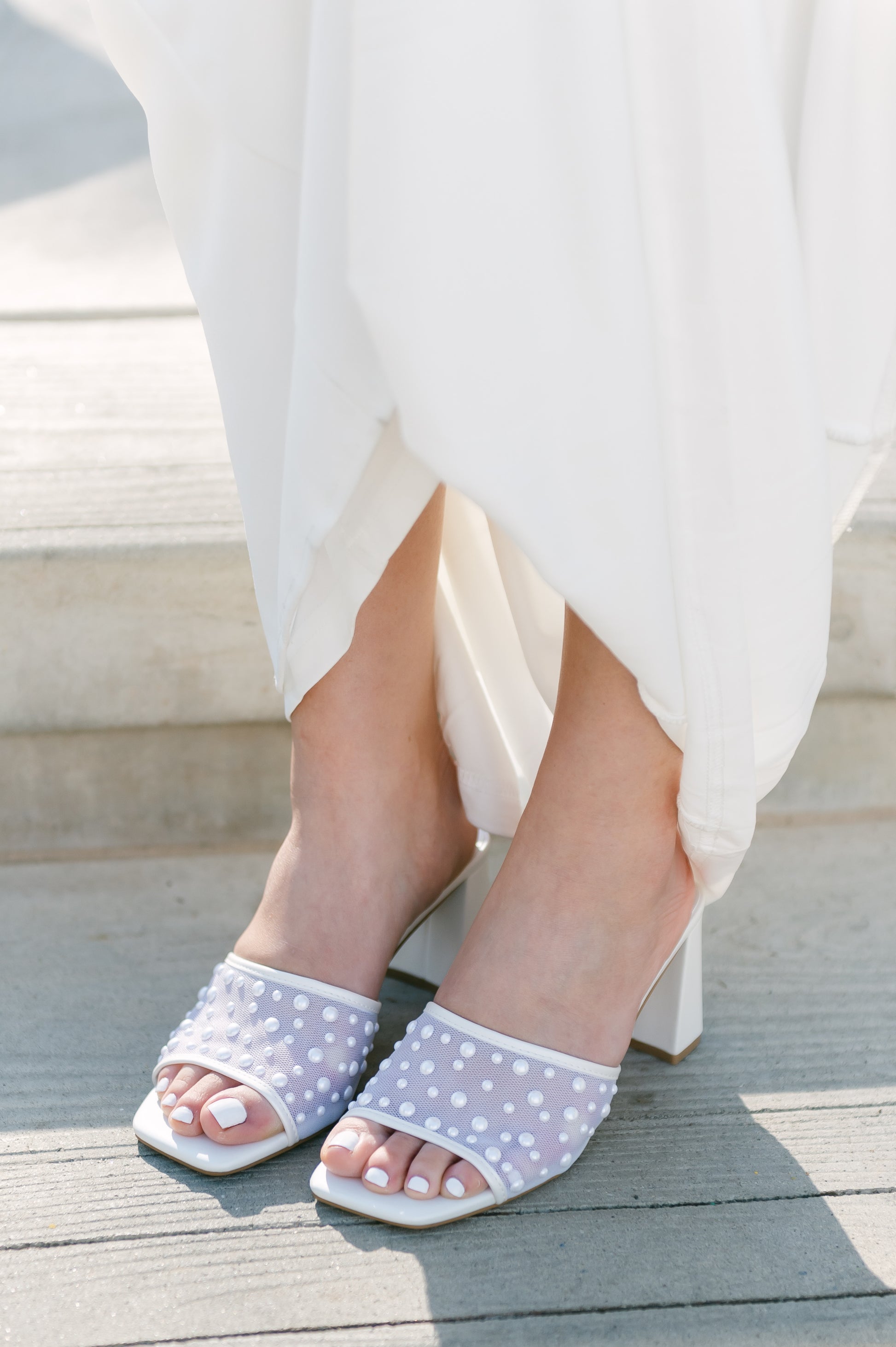 Mesh heeled white slide sandal with a 3" heel and pearls studded all over worn by a woman in a white dress