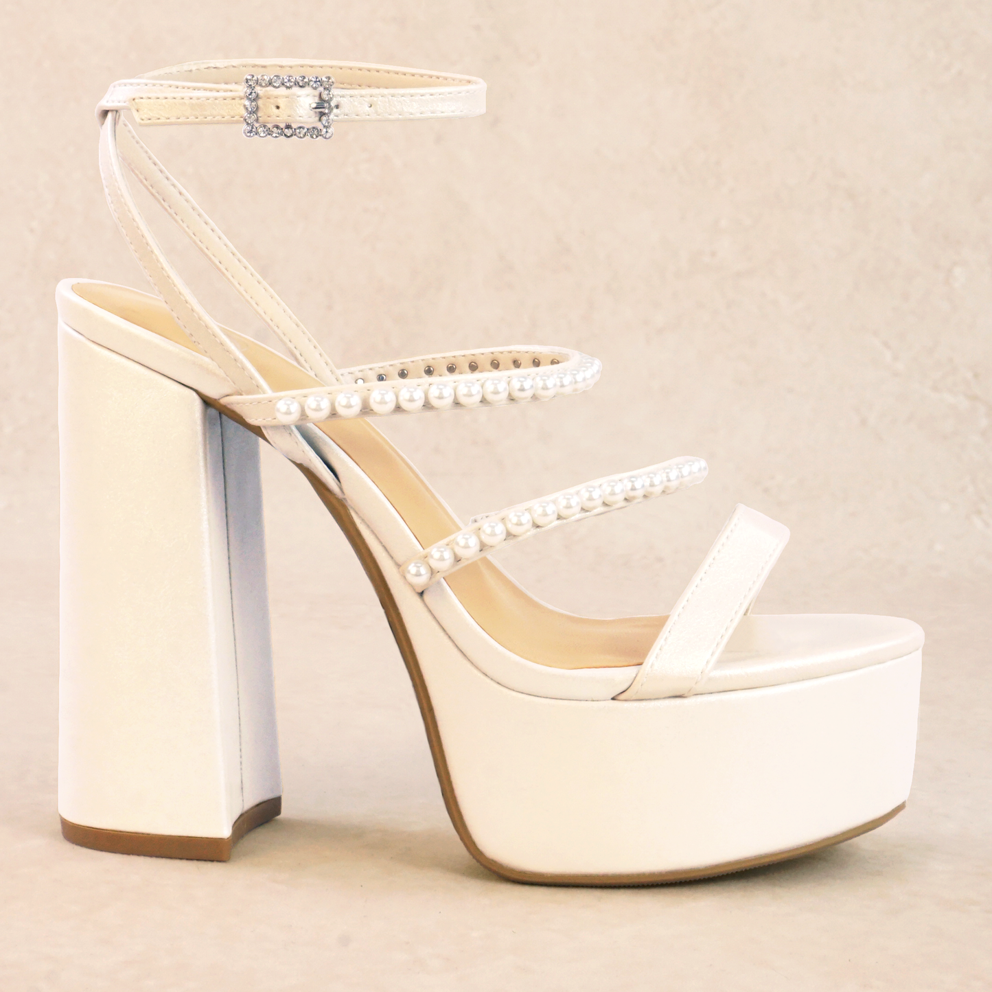 A pearlescent white platform heel with adjustable ankle strap, rhinestone buckle and pearl straps
