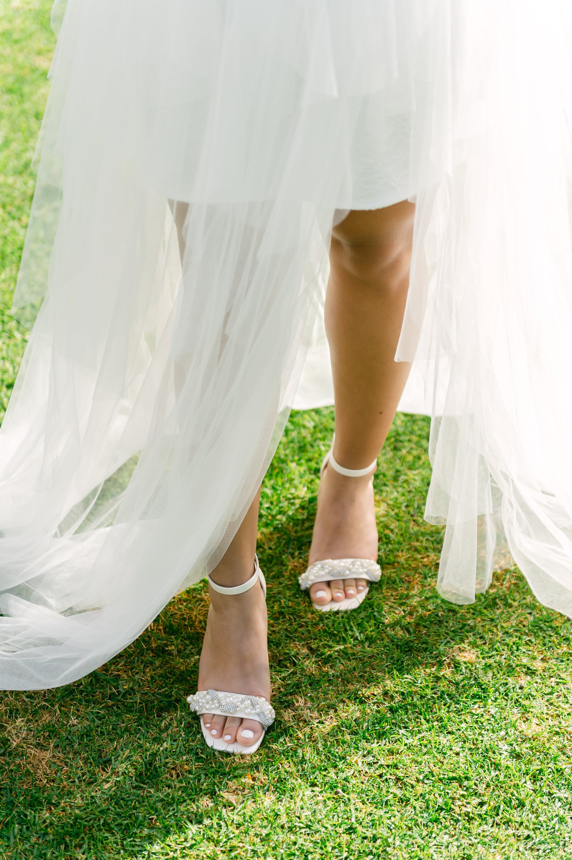Pearls and rhinestones intertwined on a white single-band 3.25" ankle strap block heel worn by a woman in a white dress