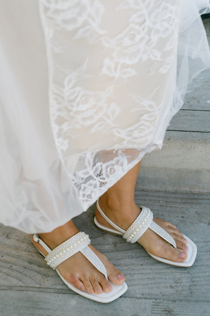 T-strap white sandal with adjustable slingback and pearl and rhinestone accents being worn